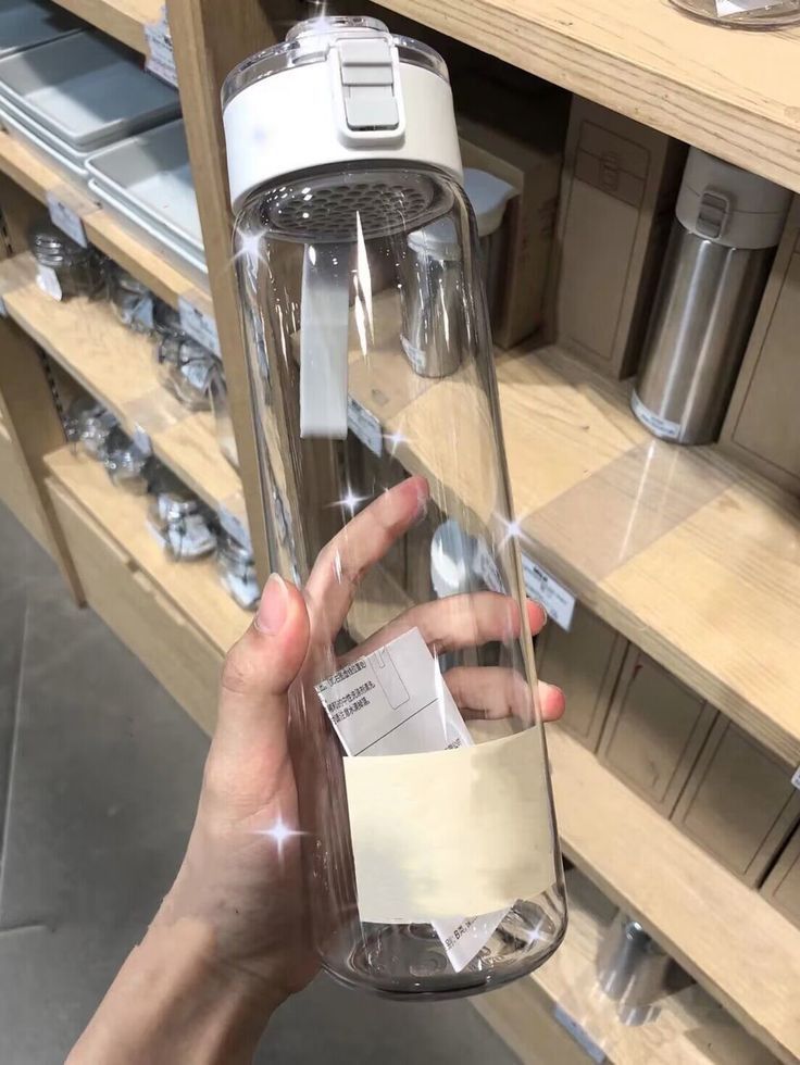 a person holding up a glass bottle with a label on it in front of some shelves