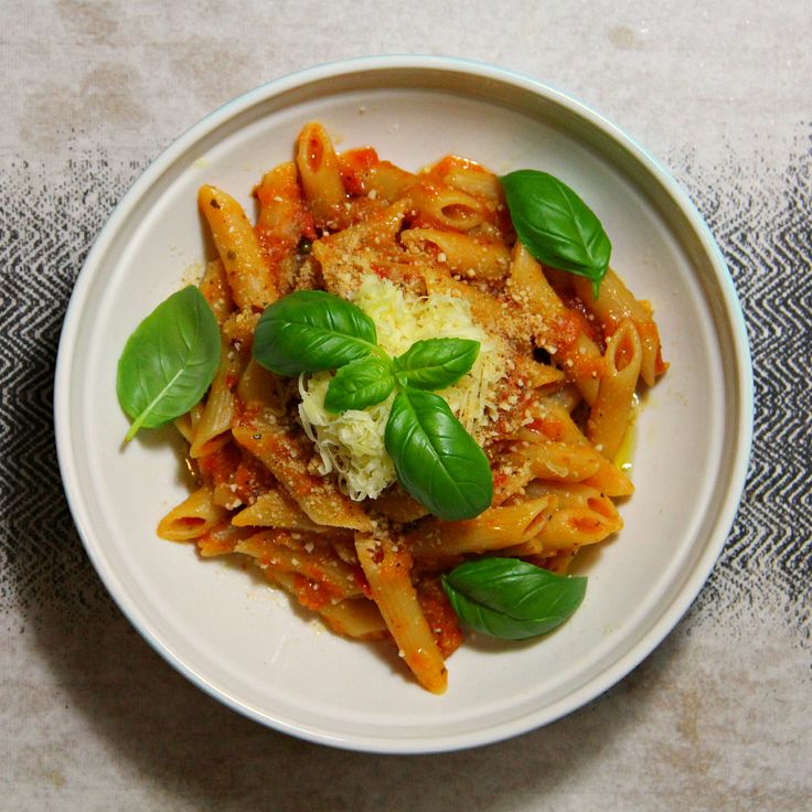 a white plate topped with pasta covered in sauce and basil