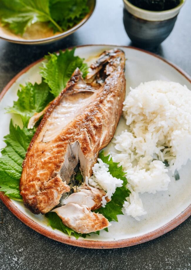 a white plate topped with fish next to rice and green leafy garnish