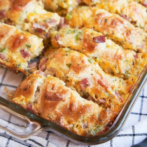 a casserole with ham and cheese in a pan on a towel next to a fork