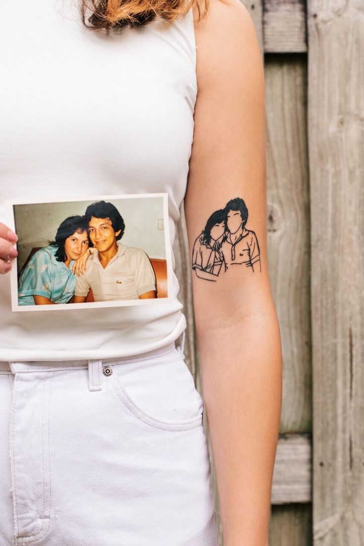 a woman with a tattoo on her left arm holding up a photo of two people