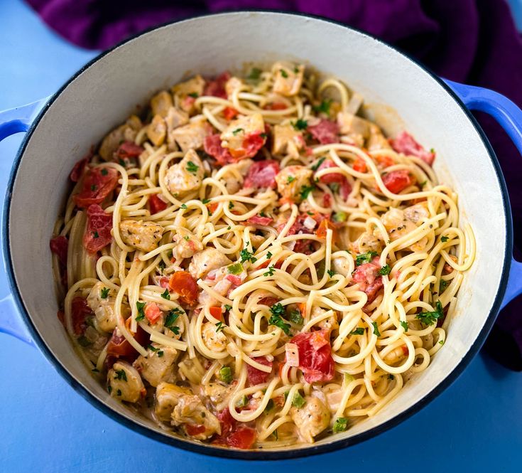 pasta with chicken, tomatoes and parsley in a blue pan on a blue table