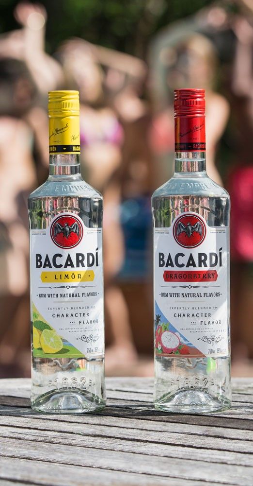 two bottles of bacardi vodka sitting on a table with people in the background