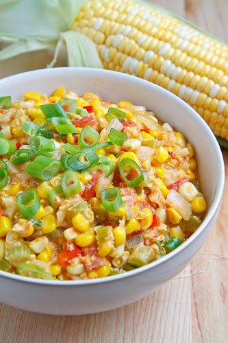 a white bowl filled with corn on the cob and green onions next to it