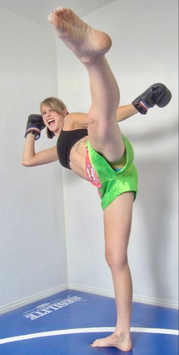 a woman in green shorts and black top doing a kickbox pose with her legs up