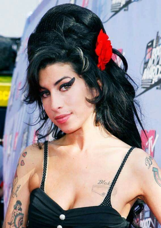 a woman in a black dress with tattoos on her arm and chest, posing for the camera