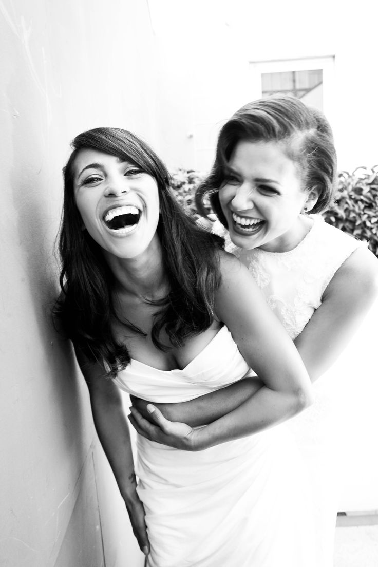 two young women are laughing and posing for a black and white photo in front of a wall