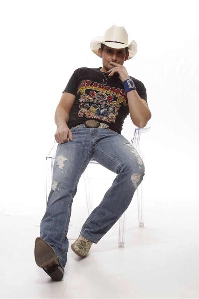 a man sitting in a chair wearing a cowboy hat and holding his hand to his mouth