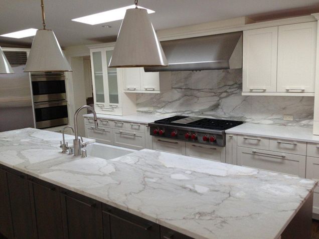 a kitchen with marble counter tops and white cabinets in the center, two pendant lights over the stove