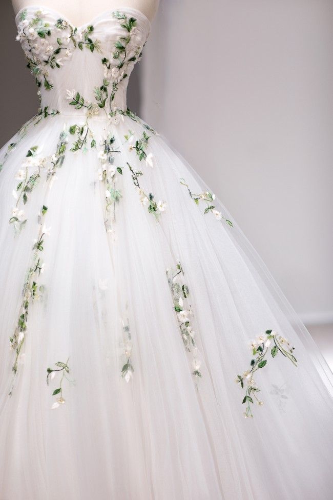 a white dress with flowers on it is displayed in front of a mannequin