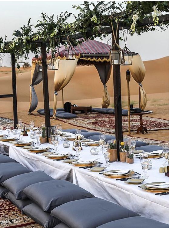 a long table set up with place settings for an outdoor dinner party in the desert