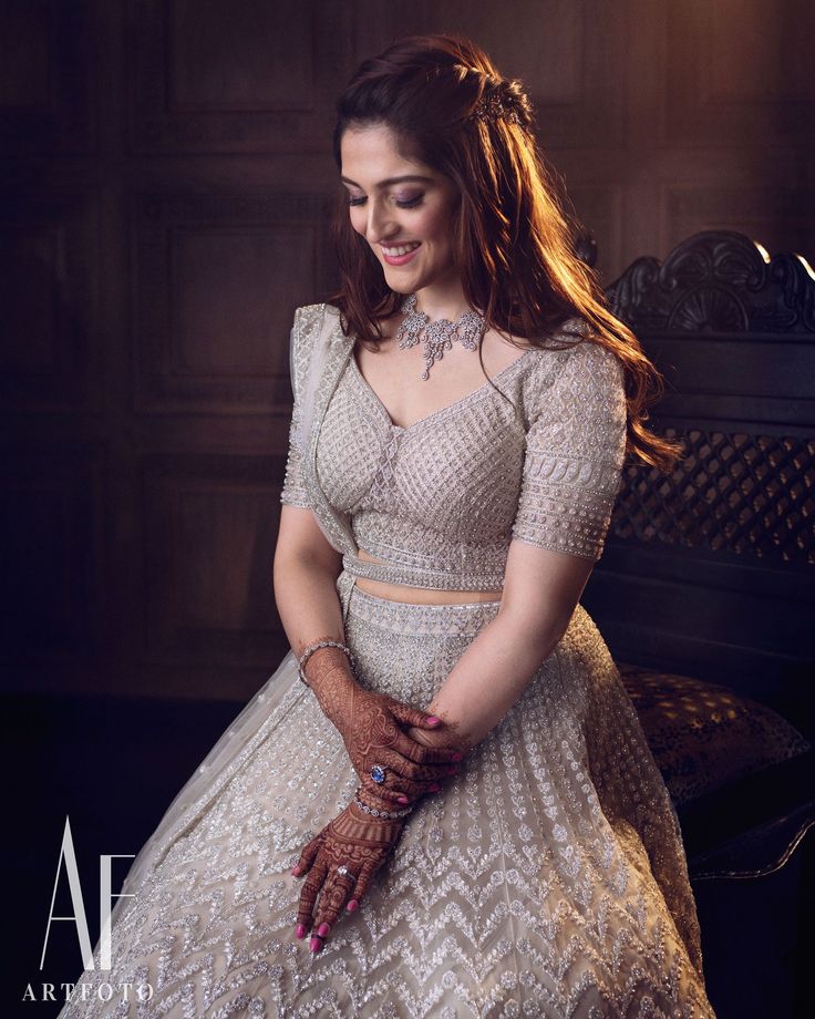 a woman sitting on top of a bench wearing a white dress and holding her hands together