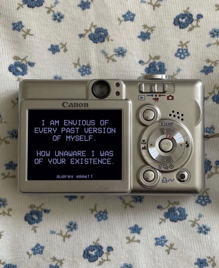 a silver camera sitting on top of a bed next to a blue flowered blanket