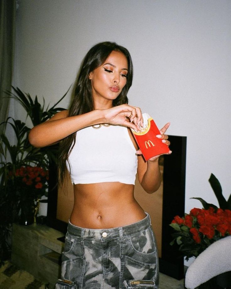 a woman in white shirt holding up a bag of chips and eating it with both hands