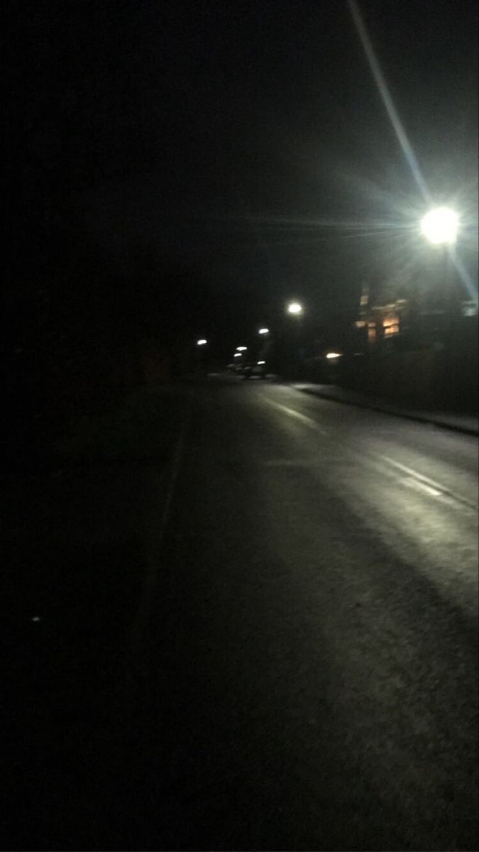 an empty street at night with the lights on and no cars driving down it in the dark