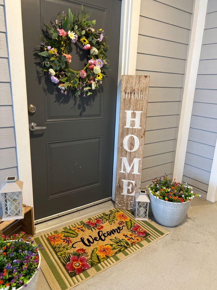 the front door is decorated with flowers and a welcome mat that says home on it