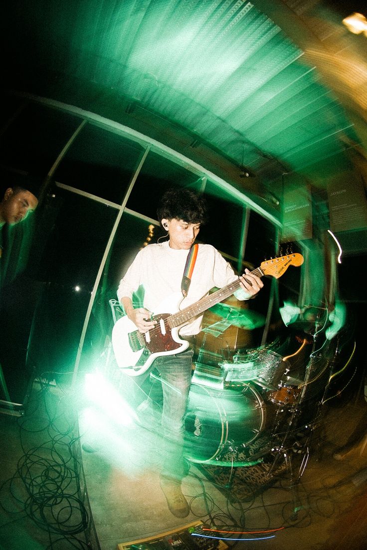 a man playing guitar while standing next to another man with a green light behind him