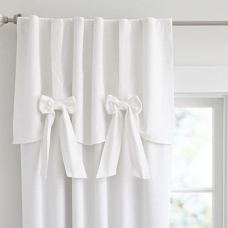 white curtains with bows hanging on them in front of a window