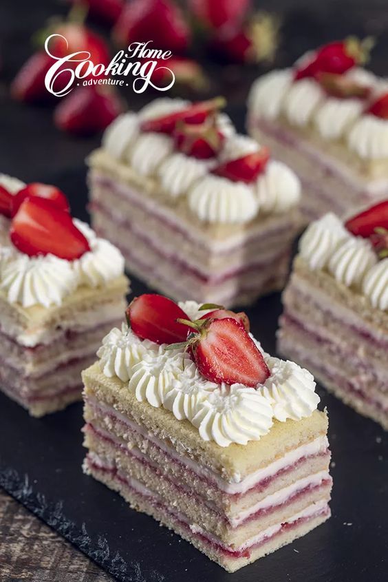 four slices of cake with white frosting and strawberries on top, sitting on a black plate