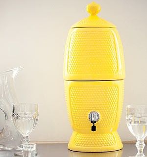 a yellow beverage dispenser sitting on top of a table next to glasses