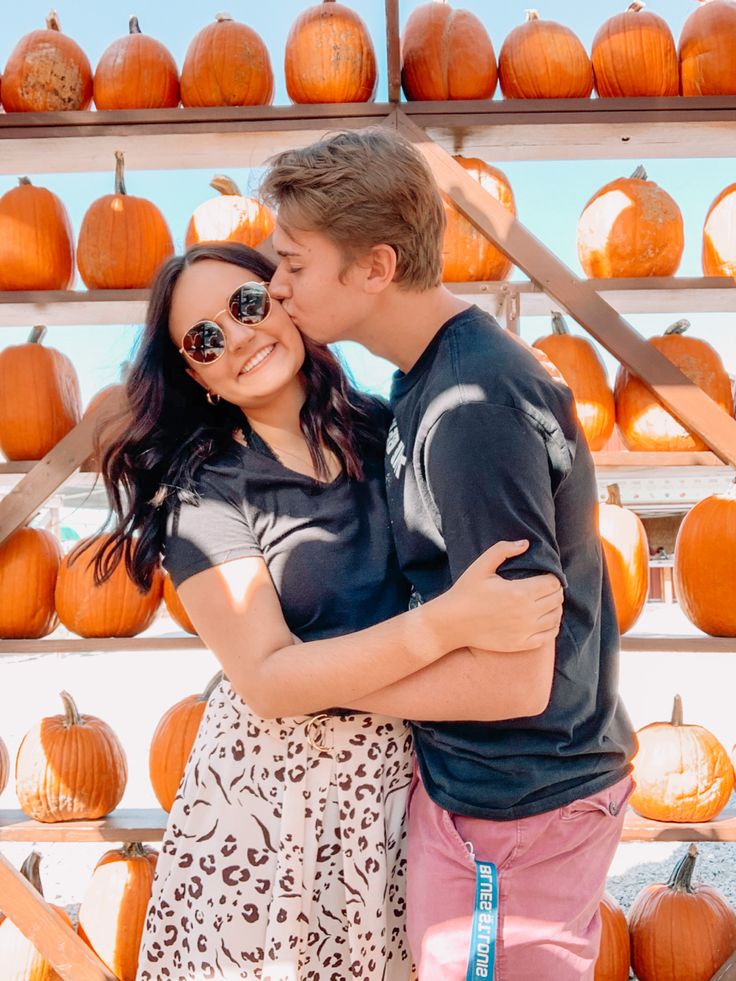 a man and woman hugging in front of pumpkins