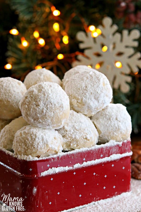 a red box filled with snowball cookies on top of a table next to a christmas tree