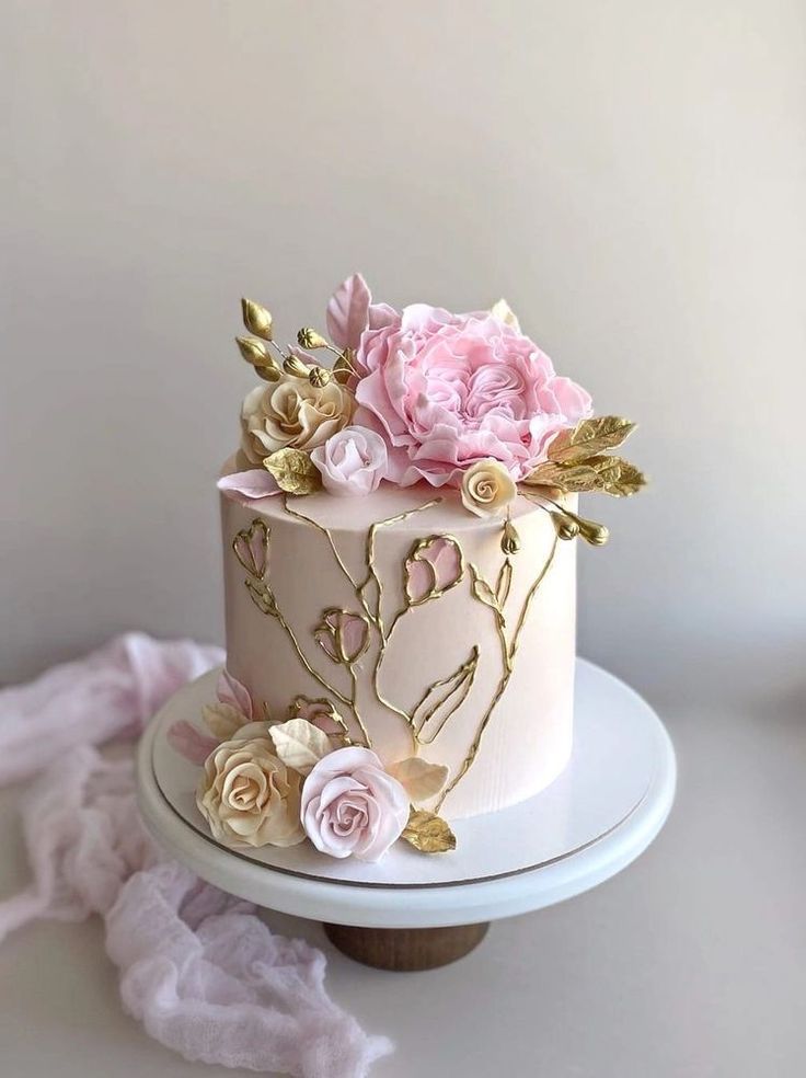 a white cake with pink flowers and gold leaves