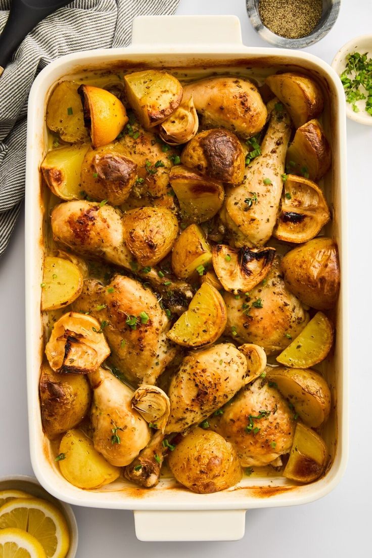 chicken and potatoes in a casserole dish with lemons, parsley on the side