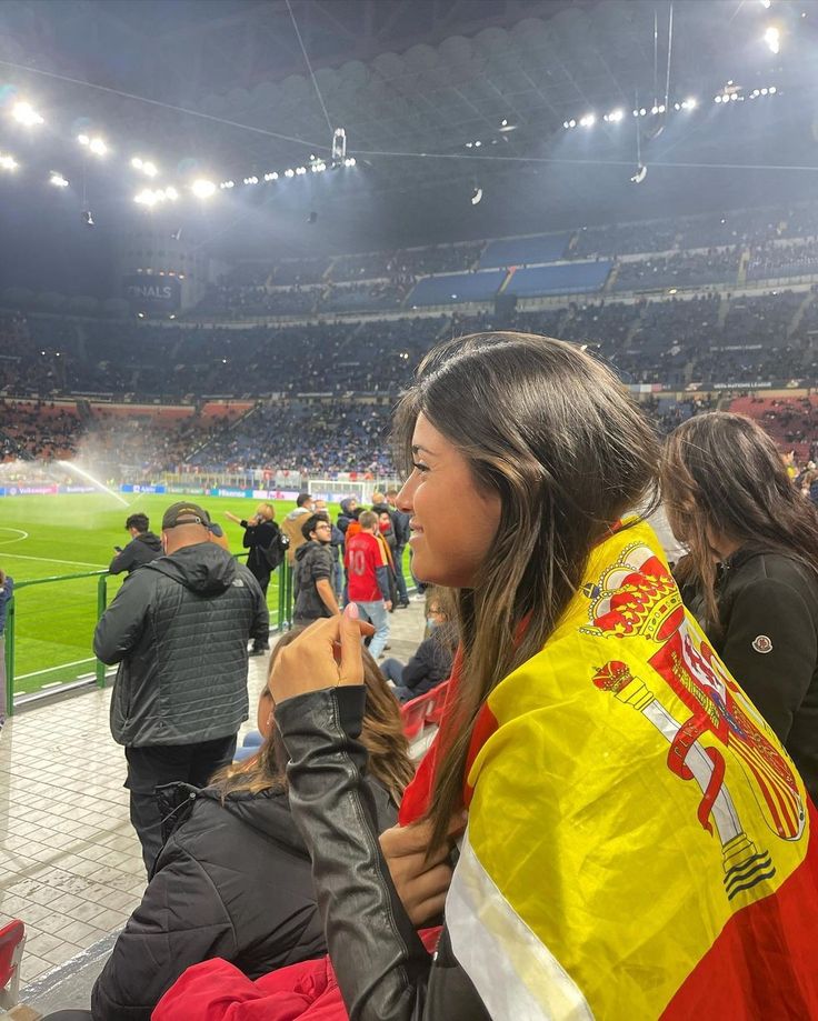 a woman is sitting in the stands at a soccer game with her yellow and red jacket