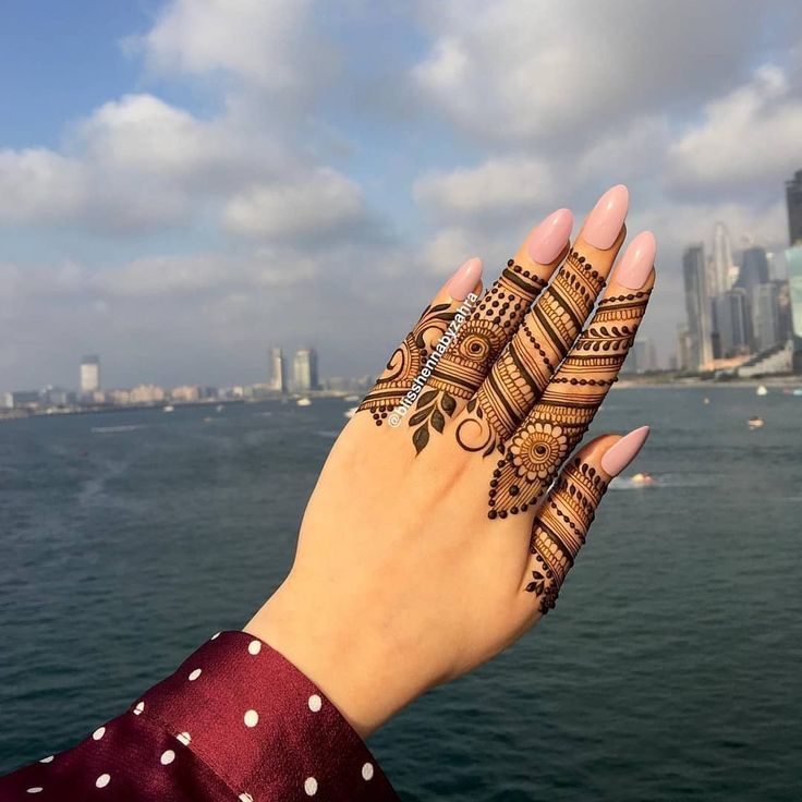 a woman's hand with henna on the water and buildings in the background