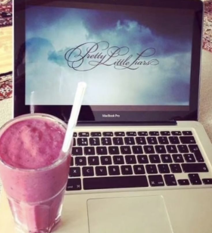 an open laptop computer sitting on top of a table next to a pink smoothie