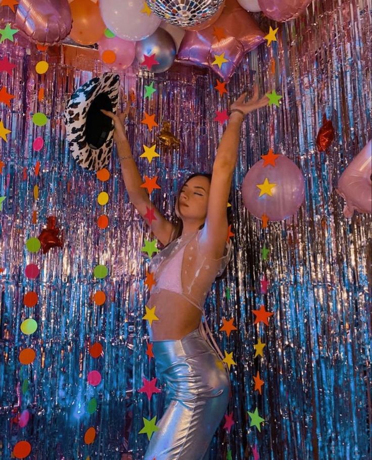 a woman in silver pants holding balloons and disco balls above her head with stars all over it