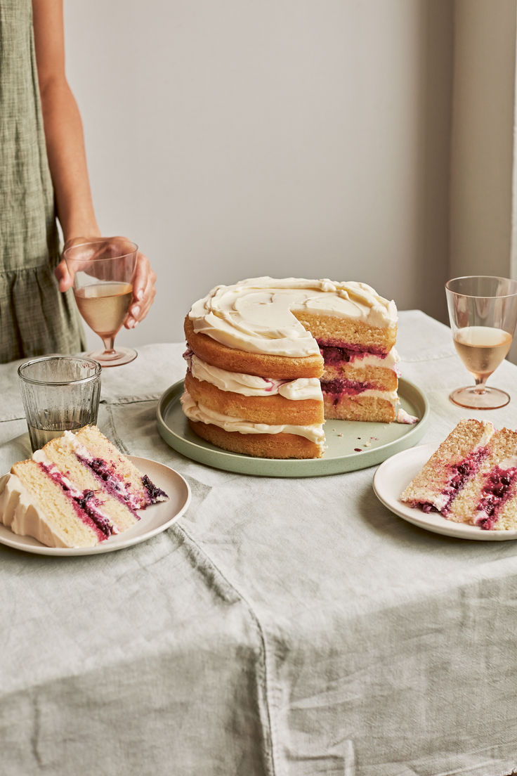 a woman holding a wine glass in front of a cake and two slices on plates