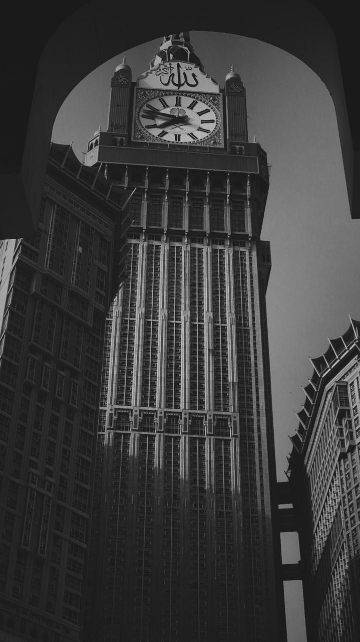 a black and white photo of a clock tower in the middle of two skyscrapers