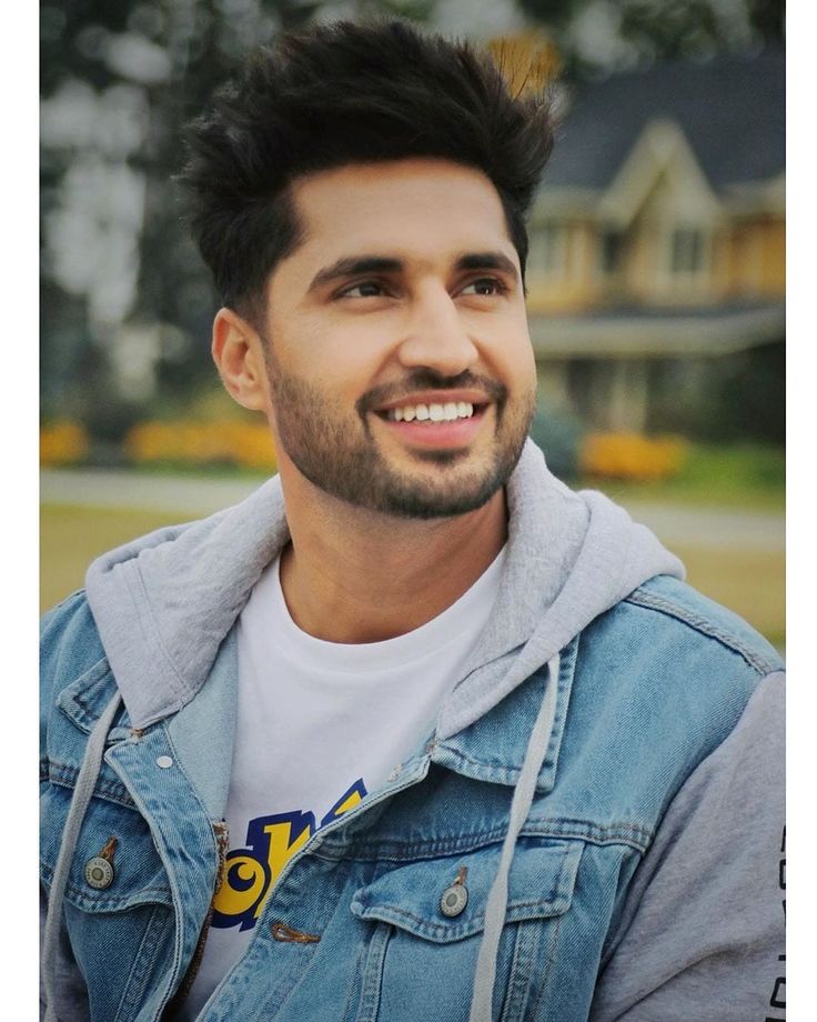 a man with a goatee smiles at the camera while wearing a denim jacket and white t - shirt