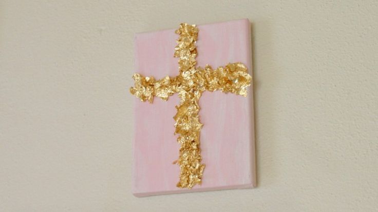 a cross made out of gold leaf on a pink and white wall with a light pink background