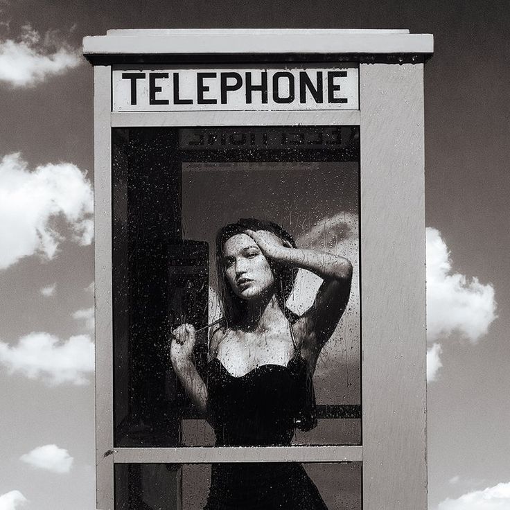 a black and white photo of a woman in front of a telephone booth with the words telephone on it