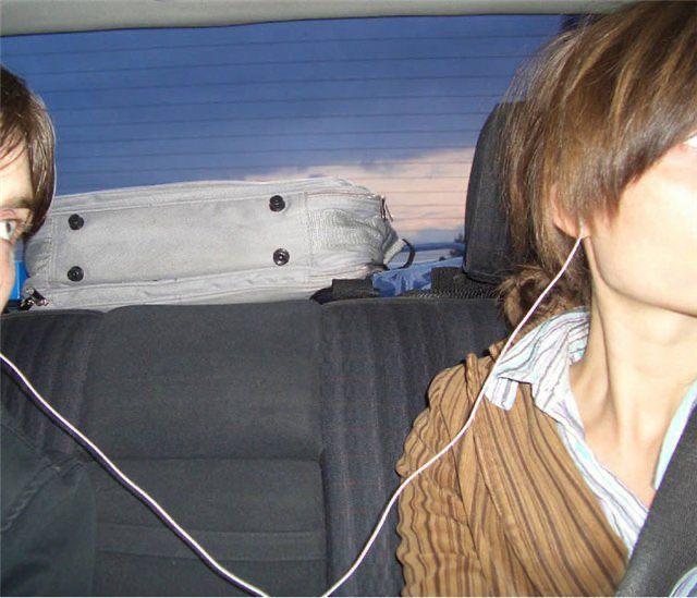 two people sitting in the back seat of a car with headphones hanging from their ears