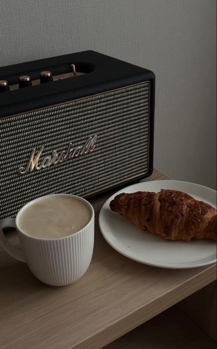 a croissant and cup of coffee sit on a table next to an amp