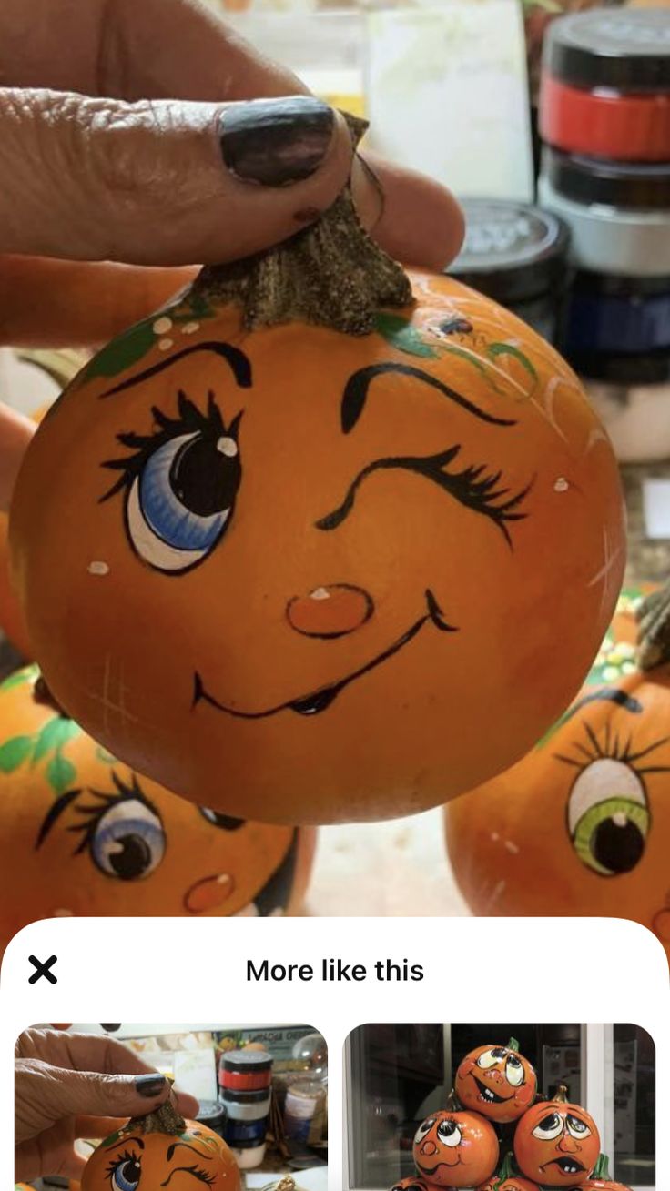 someone is holding up some pumpkins with faces painted on them, and they are being held by their hands