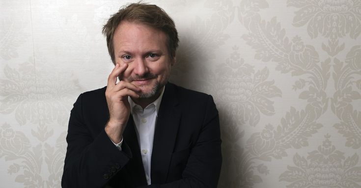 a man in a suit leaning against a wall with his hand on his face and looking at the camera