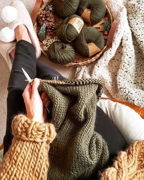 a person knitting yarn in a basket on the floor next to some balls of yarn