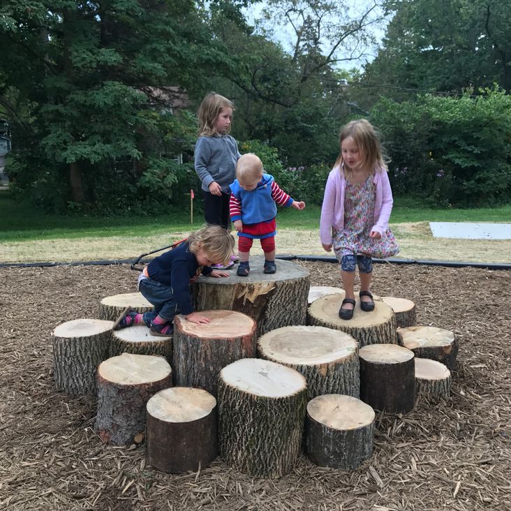 three children playing on a tree stump in a park with some logs stacked around them