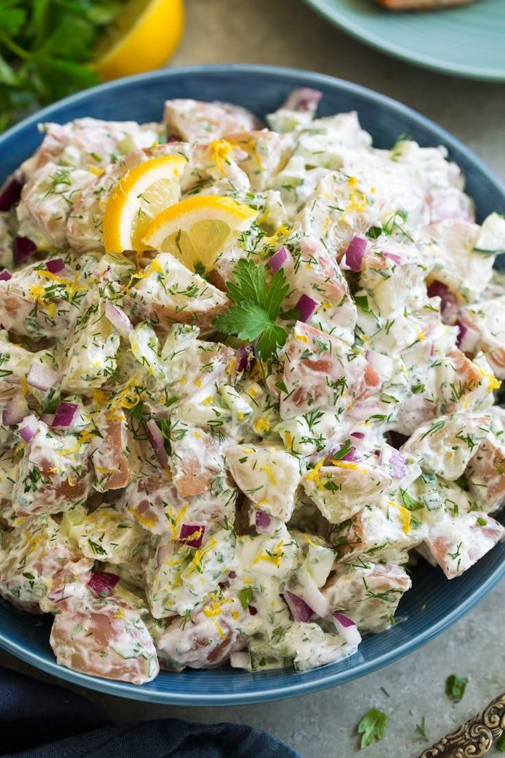 a blue bowl filled with chicken salad next to lemon wedges and parsley on the side