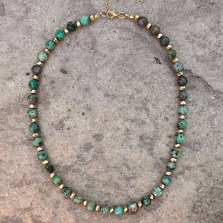 Discover the sophisticated elegance of African Turquoise with this beaded necklace, a perfect blend of traditional charm and contemporary style. This piece features an array of 8mm African Turquoise beads, known for their unique, earthy hues and intricate patterns. Alternating with the turquoise, 6mm gold-plated faceted spacers add a touch of luxury, making the necklace versatile for both casual and formal wear. 8mm African Turquoise 6mm gold-plated faceted spacers 18" necklace with a 3" extende Green Chrysocolla Round Bead Necklaces, Green Chrysocolla Round Beads Necklace, Turquoise Chrysocolla Round Beads Necklace, Turquoise Chrysocolla Necklace With Round Beads, Handmade Turquoise Emerald Necklace With Round Beads, Turquoise Necklace With Round Chrysocolla Beads, Turquoise Emerald Necklace With Round Natural Stones, Bohemian Emerald Necklace With Round Beads, Earthy Turquoise Beaded Necklace