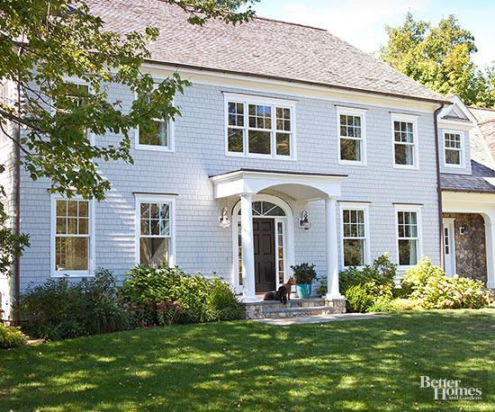 a large blue house with white trim and windows on the front, sitting in a lush green yard