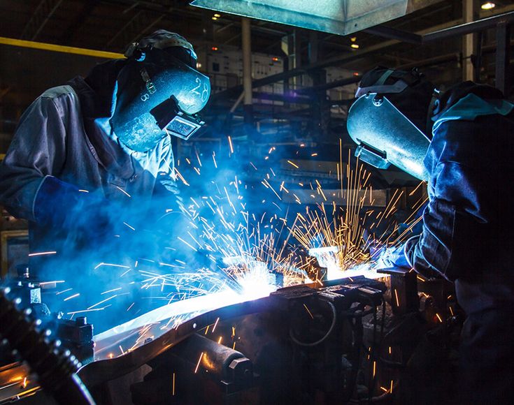 two welders working on an assembly line in a factory with sparks coming from their hands