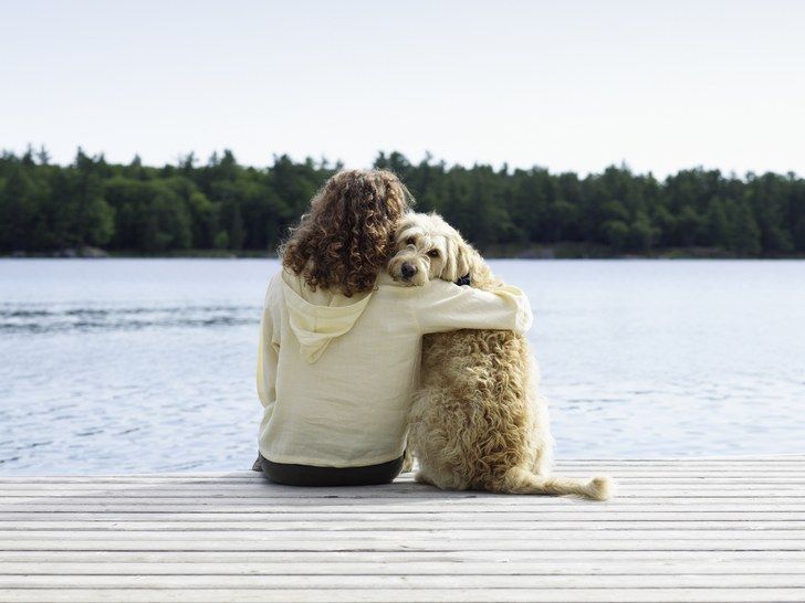 a woman sitting on a dock hugging her dog