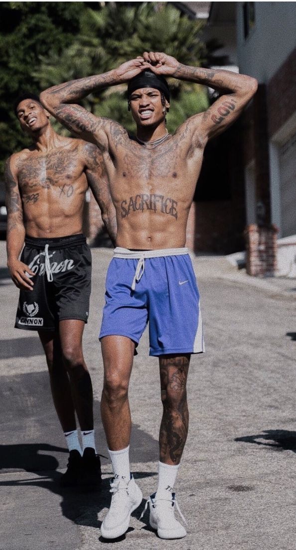 two men walking down the street with tattoos on their bodies