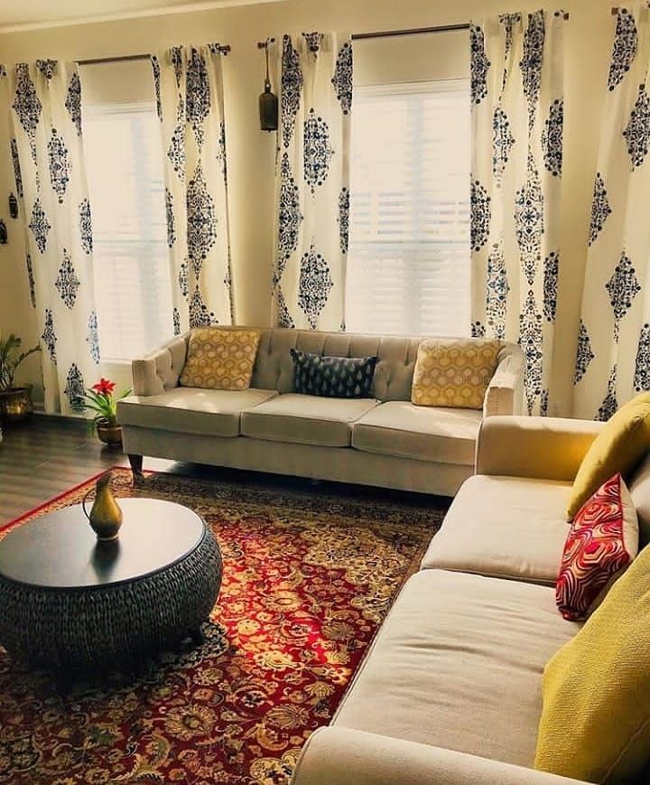 a living room filled with furniture and windows covered in drapes, rugs and curtains